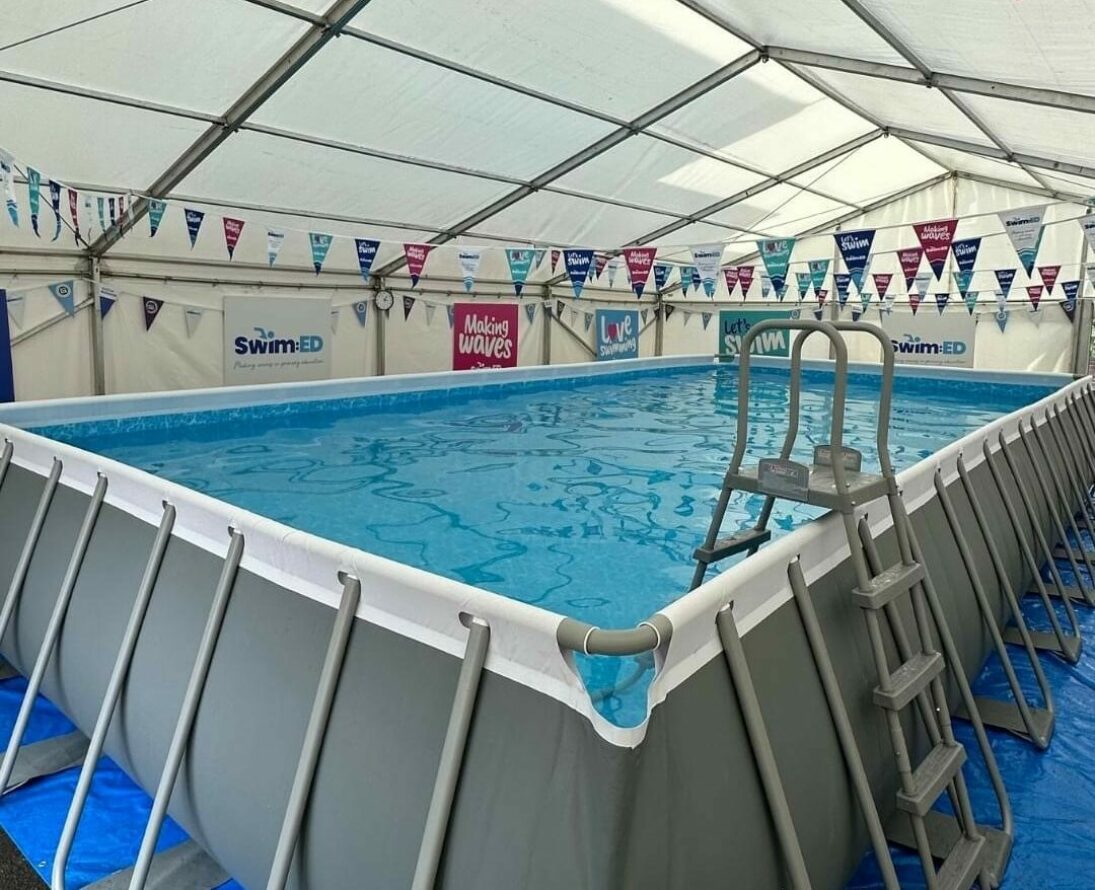 Image of our pop up pool, filled with water in the tent. There's Swim:ED bunting across the width of the tent.